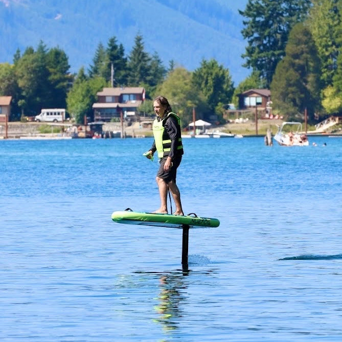 Person on a hydrofoil board on a lake with mountains and buildings in the background